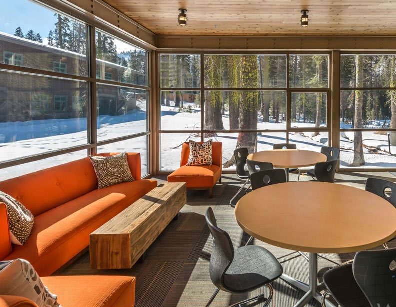 A warm timber-framed common room at Sugar Bowl with tall windows looking out on the snowy forest.