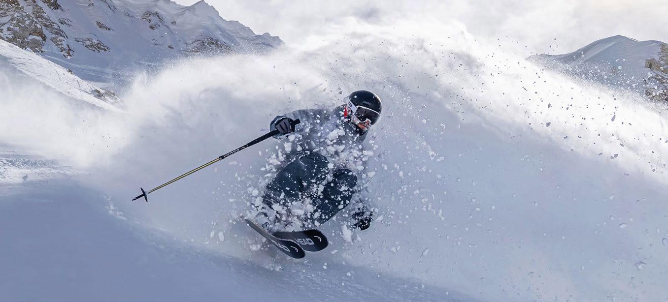 A skier arcing through deep powder, snow exploding around them.