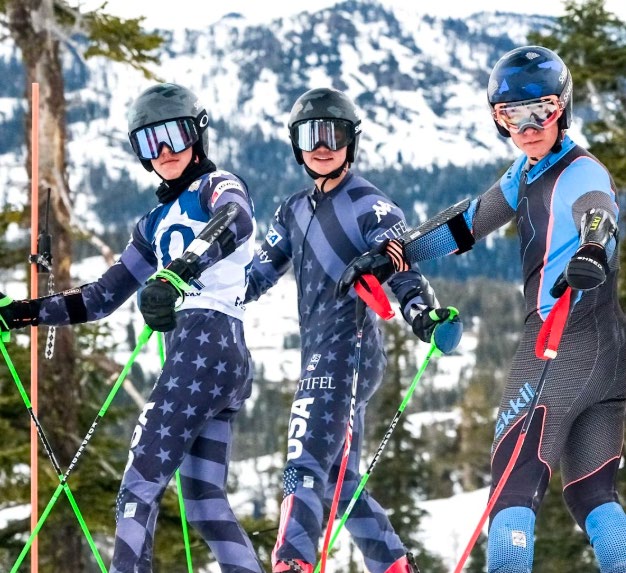 Three Sugar Bowl Academy alpine racers in speed suits at the top of a course, Sierra ridgelines behind them.